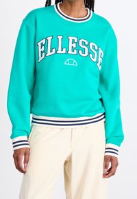 Turquoise sweatshirt met "ELLESSE" logo, geribbelde kraag en manchetten met witte en marineblauwe strepen. Zachte textuur, ontspannen pasvorm, casual ontwerp.