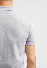 Szara koszulka polo z krótkimi rękawami, prążkowanym kołnierzykiem i fakturowaną tkaniną. Czysty, minimalistyczny design bez widocznych logo ani wzorów.