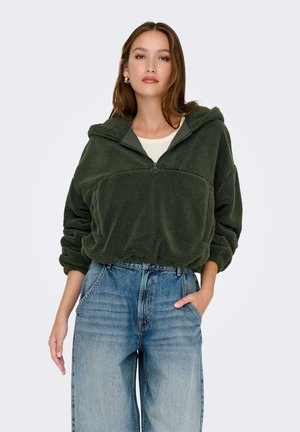 Sweat à capuche en polaire verte avec un zip à moitié, finition texturée et poche avant ; associé à un jean bleu clair taille haute.