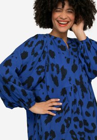 Robe bleue avec motif animal noir, manches froncées et décolleté en V. Tissu texturé avec une coupe ample et un design mi-long.