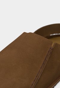 Κοντινό πλάνο καφέ σουέντ παπουτσιού χωρίς κορδόνια, που αναδεικνύει την ομαλή υφή και τις λεπτομερείς ραφές κατά μήκος της πλευράς.