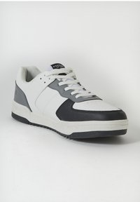Fehér sneaker szürke és fekete részletekkel. Simább bőr felsőrésszel, párnázott bokarésszel és texturált tapadós gumitalppal rendelkezik.