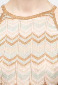 Κοντινό πλάνο πλεκτού αμάνικου τοπ με μπεζ, λευκό και ανοιχτό μπλε μοτίβο ζιγκ-ζαγκ και στρογγυλή λαιμόκοψη.