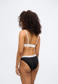 Mutande nere a vita alta con fascia in vita bianca firmata, accompagnate da un reggiseno bianco regolabile con chiusura a gancio sul retro.