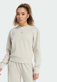 Cremefarbenes Sweatshirt mit rundem Ausschnitt, gerippten Bündchen und einem Logo auf der Brust. Weiches Material, lässige Passform, kombiniert gut mit passenden Hosen.