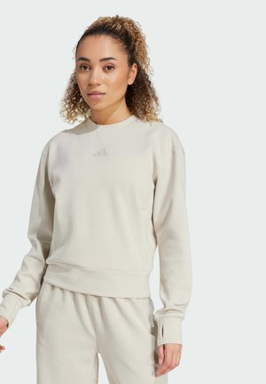 Cremefarbenes Sweatshirt mit rundem Ausschnitt, gerippten Bündchen und einem Logo auf der Brust. Weiches Material, lässige Passform, kombiniert gut mit passenden Hosen.