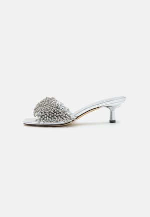 Mule argento con tacco basso e cinturino piatto, adornato con strass a grappolo per texture e dettaglio; tacco corto per supporto.