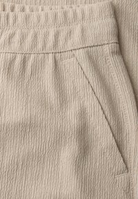 Nærbillede af beige tekstureret stofbukselomme med elastisk linning og subtilt lodret stribemønster.