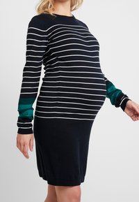 Těhotenské šaty v námořnick é modři s bílými vodorovnými pruhy. Dlouhé rukávy mají tyrkysový akcent. Měkká pletenina. Přiléhavé kolem pupku.