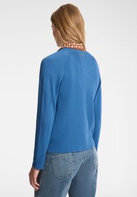 Maglione blu lavorato a maglia con texture a coste e maniche lunghe, dotato di un collare decorato in marrone e un piccolo logo sulla parte posteriore.