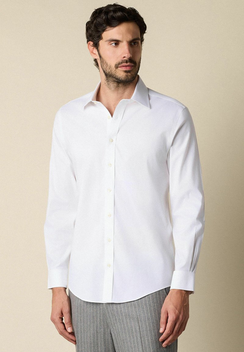 Witte langemouwhemd met een button-down kraag, een gladde textuur en witte knopen, gecombineerd met gestreepte grijze broeken.