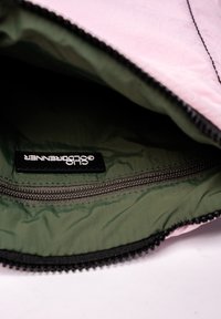 Interieur van een roze stoffen tas met een gladde olijfgroene voering, voorzien van een ritssluiting en een zwart label met witte tekst.