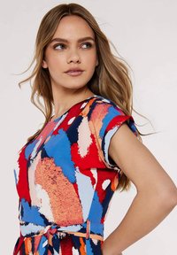 Farbiger Dress mit einem lebhaften abstrakten Muster in Rot-, Blau- und Pfirsichtönen, mit kurzen Ärmeln und einem Bindegürtel-Akzent in der Taille.