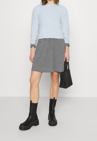 Suéter de canalé azul claro, falda de espiga en blanco y negro, botines gruesos negros hasta el tobillo, y un pequeño bolso negro.