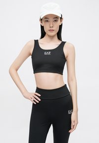 Fekete sportos crop top és magas derekú leggings, sima anyagból, mindkét darabon fehér EA7 logóval.