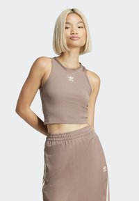 Rjava rebrasta kratka majica brez rokavov z okroglim izrezom. Na sprednji strani ima bel logotip "adidas". Ujemajoče se rjave hlače.