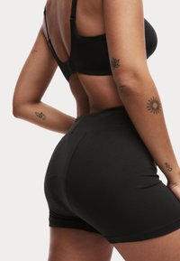 Ensemble de soutien-gorge et short noir, sans couture, affiché de dos. Comprend un tissu doux, un ajustement précis et des coutures discrètes sans logos visibles.
