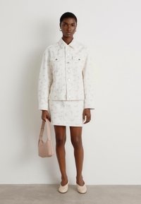 Veste en denim blanc avec des motifs floraux, mini jupe blanche et accessoires beiges ; texture lisse ; design minimaliste ; silhouette ajustée.