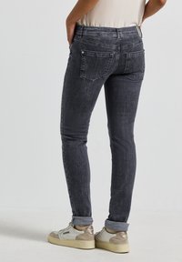 Jean skinny gris foncé avec un effet délavé, design à cinq poches et ourlet effiloché. Porté avec des bords roulés et des baskets.