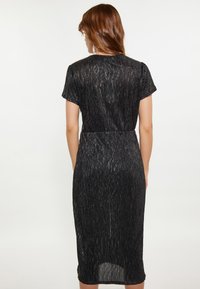 Rochie neagră cu mâneci scurte, având o textură pliată și o talie ajustată. Design de lungime medie, cu un finisaj neted și strălucitor.