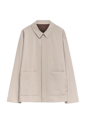 Giacca beige chiaro con colletto a punta, maniche lunghe, due tasche frontali e dettagli di cucitura minimalisti sui lati. Tessuto liscio.