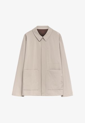 Helle beige Jacke mit Spitzkragen, langen Ärmeln, zwei Fronttaschen und minimalistischem Steppdetail an der Seite. Glatte Textur.