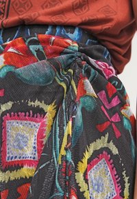 Un tessuto a fantasia floreale colorato presenta vivaci design rossi, gialli e blu su uno sfondo nero con drappeggi testurizzati.