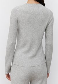 Top gris acanalado de manga larga con escote redondo y bajo ligeramente asimétrico, con una textura suave y silueta ajustada.