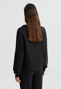 Sweatshirt noir avec une coupe décontractée, présentant une rayure verticale texturée au centre du dos et des poignets et un ourlet côtelés.