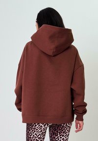 Felpa oversize marrone con un ampio cappuccio, polsini e fondo a costine. Indossata sopra leggings con stampa leopardo. Tessuto con una texture liscia.