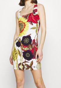 Robe mini florale mettant en avant un lumineux tournesol et des pétales sombres. Fabriquée en tissu lisse avec un design ajusté et un décolleté carré.