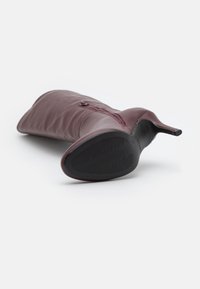 Botte à talon haut en cuir bordeaux avec un embout pointed, dotée d'une fermeture éclair sur le côté et d'une semelle en caoutchouc texturé noir.