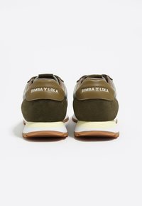 Zapatillas verdes y marrones con parte superior de ante, que cuentan con un logo blanco en el talón y una suela de varias capas en crema y marrón claro.