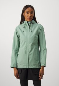 Veste imperméable vert menthe avec capuche, présentant une fermeture éclair à l'avant, des cordons de serrage réglables et un logo noir en accent sur la manche.