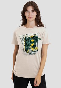 Beige cotton t-shirt featuring a green and yellow illustrated character design with black accents, displayed against a textured background.
