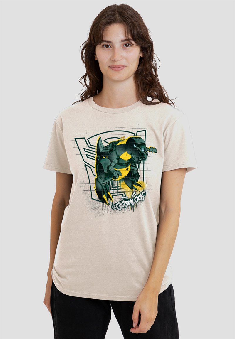 Beige cotton t-shirt featuring a green and yellow illustrated character design with black accents, displayed against a textured background.