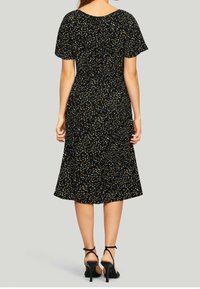 Svart klänning med korta ärmar, prydd med ett blommönster i gult och vitt. Utsvängd design och medellång kjol med en figurnära midja.