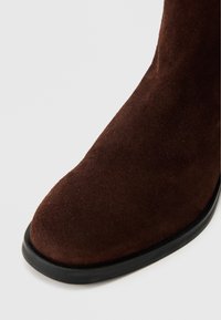 Barna velúr bokacsizma lekerekített orral és sima fekete gumi talppal. Az anyag puha és enyhén szálkásnak tűnik.