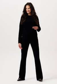 Crop top noir à manches longues, associé à un pantalon slim évasé, le tout en texture douce et veloutée. Coup élégant avec des détails de design subtils.