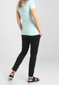 T-shirt ajustée bleu clair, à manches courtes, associée à un pantalon slim noir et des sandales noires avec une boucle dorée sur un fond blanc.