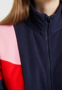 Flísová bunda s námořnickou modrou, růžovou a červenou barevnou kombinací. Vysoký límec, plný zip, texturovaná látka. Obsahuje čisté švy a jednoduchý design.
