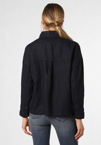 Svart linnejacka med avslappnad passform, knäppta ärmslut och sömdetalj över ryggen, kombinerad med åtsittande denimjeans.