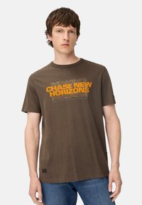 Brun kortærmet t-shirt lavet af bomuld, med en orange grafisk tekst "CHASE NEW HORIZONS" og bølgende linjemønstre på fronten.