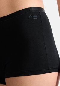 Shorts en coton noir avec une texture lisse, présentant une taille basse et des bords cousus. Le logo de la marque est subtilement imprimé en gris.