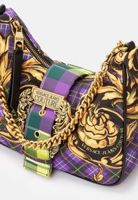 Borsa viola e nera con motivo floreale, catena dorata e una distintiva tracolla a quadri in verde e viola. Dettaglio con cerniera incluso.