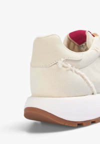 Sneaker in tela color crema con superficie testurizzata, suola intermedia bianca e suola esterna in gomma marrone. Presenta un tacco leggermente arrotondato e dettagli di cucitura.