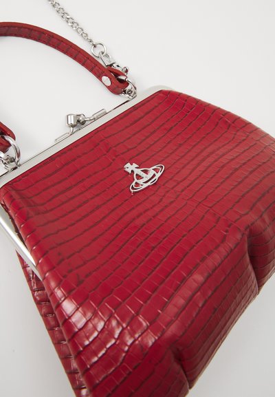 Bolsa de mão em vermelho com textura de crocodilo, com fecho prateado e alça de corrente. Apresenta um formato estruturado e um logo em destaque na parte frontal.