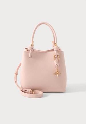 Sac à main rose doux avec deux poignées, une bandoulière amovible et un charm triangulaire doré suspendu à une poignée.