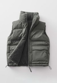 Veste matelassée gris foncé avec fermeture éclair frontale, deux poches à rabat et doublure en polaire douce, partiellement ouverte sur un fond clair.