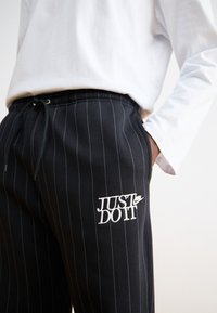 Μαύρα παντελόνια φόρμας με ρίγες από μαλακό ύφασμα, διαθέτουν ελαστική μέση και μια λευκή κεντημένη λογότυπο "Just Do It" στο μηρό.